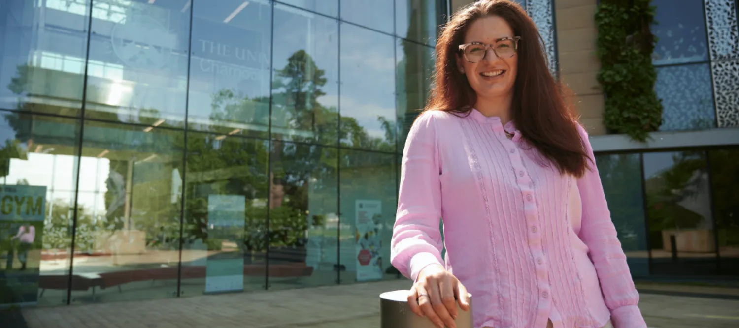 Woman smiling, wearing pink shirt and standing outside University of Edinburgh building.