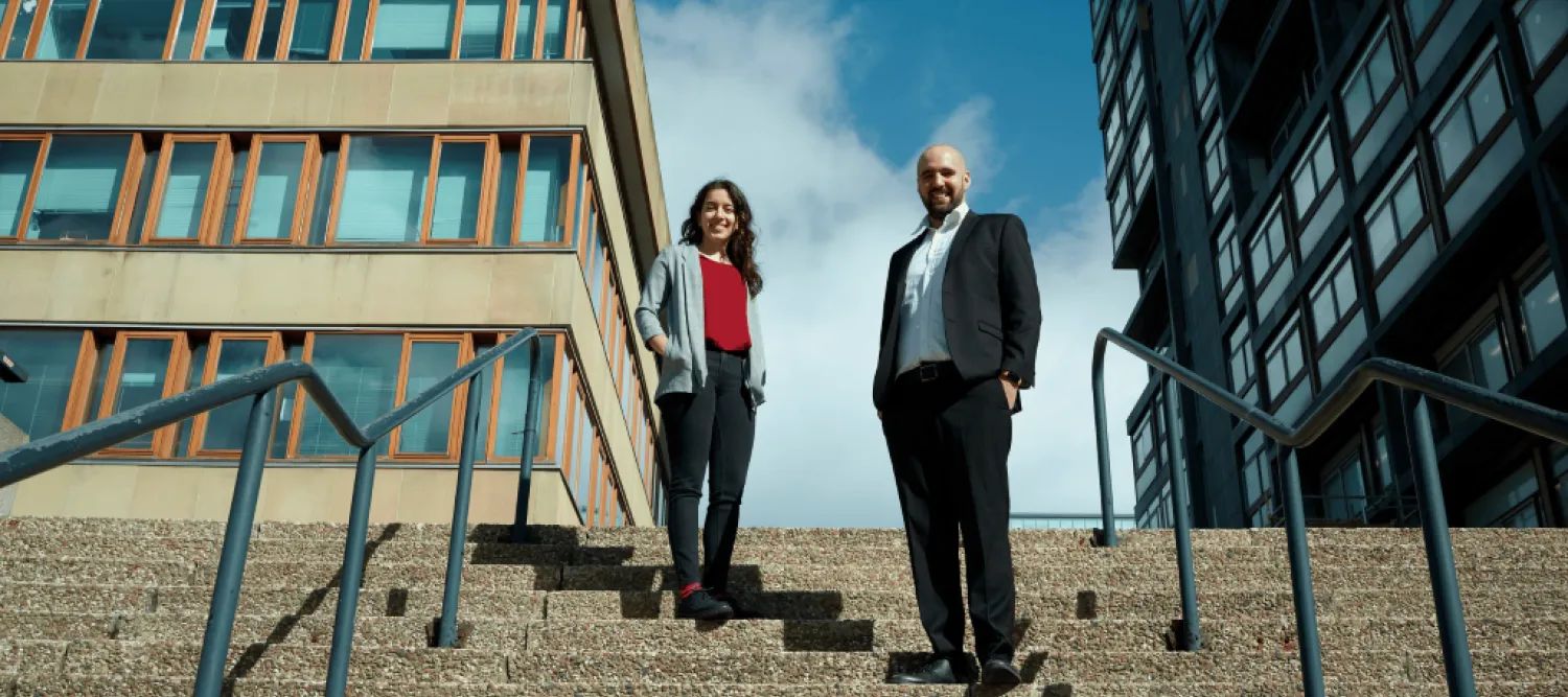 A woman and man stand on stairs with blue sky behind them. 