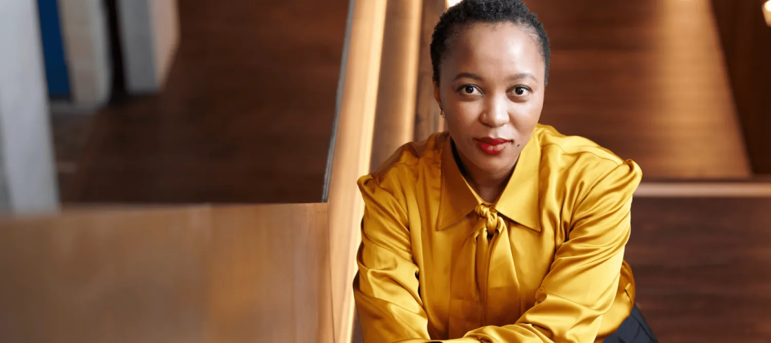 Woman wearing gold blouse, leaning on stairs.