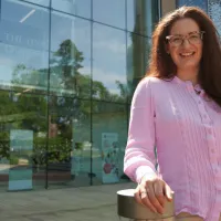 Woman smiling, wearing pink shirt and standing outside University of Edinburgh building.