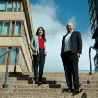 A woman and man stand on stairs with blue sky behind them. 