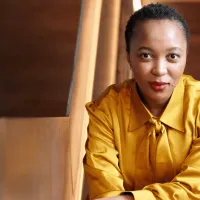 Woman wearing gold blouse, leaning on stairs.