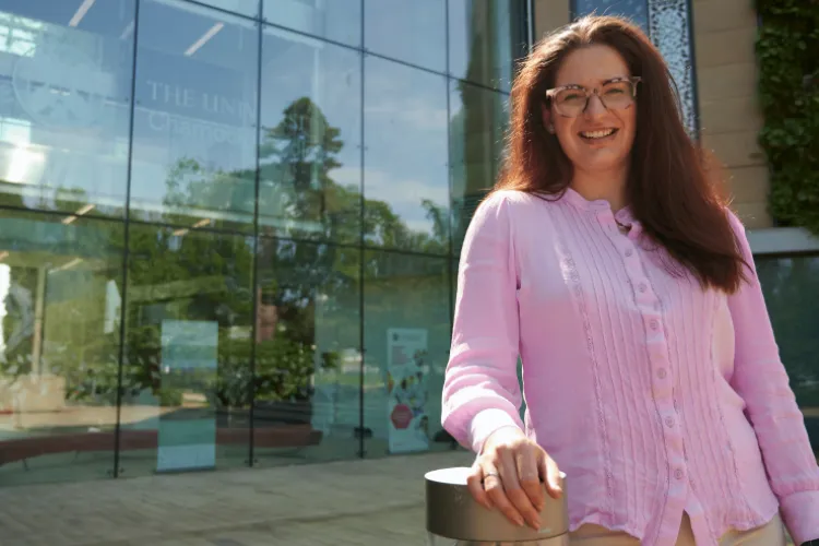 Woman smiling, wearing pink shirt and standing outside University of Edinburgh building.