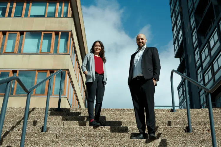 A woman and man stand on stairs with blue sky behind them. 