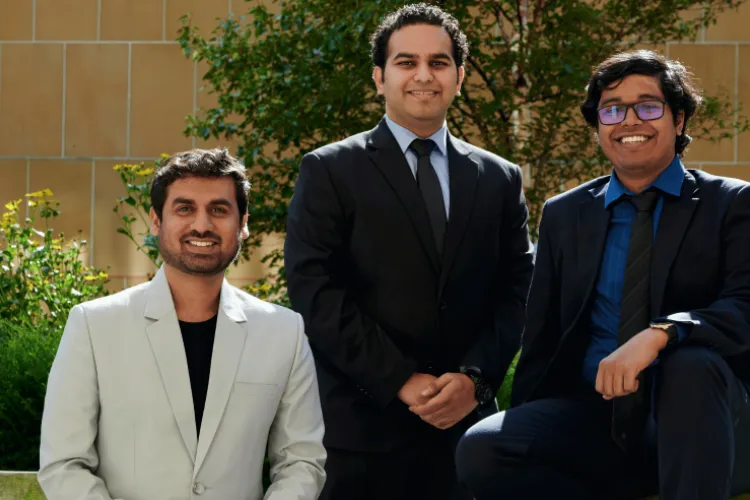 Three men, wearing suits, sat outside on a bench. 