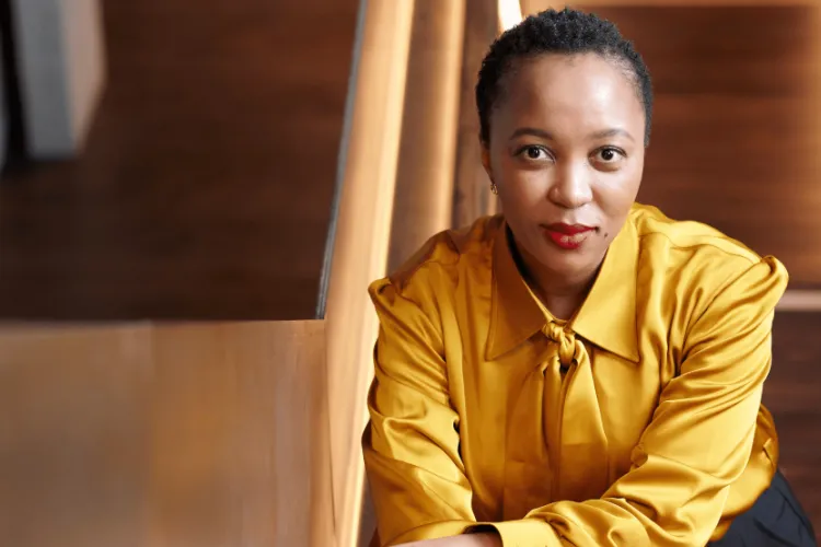 Woman wearing gold blouse, leaning on stairs.