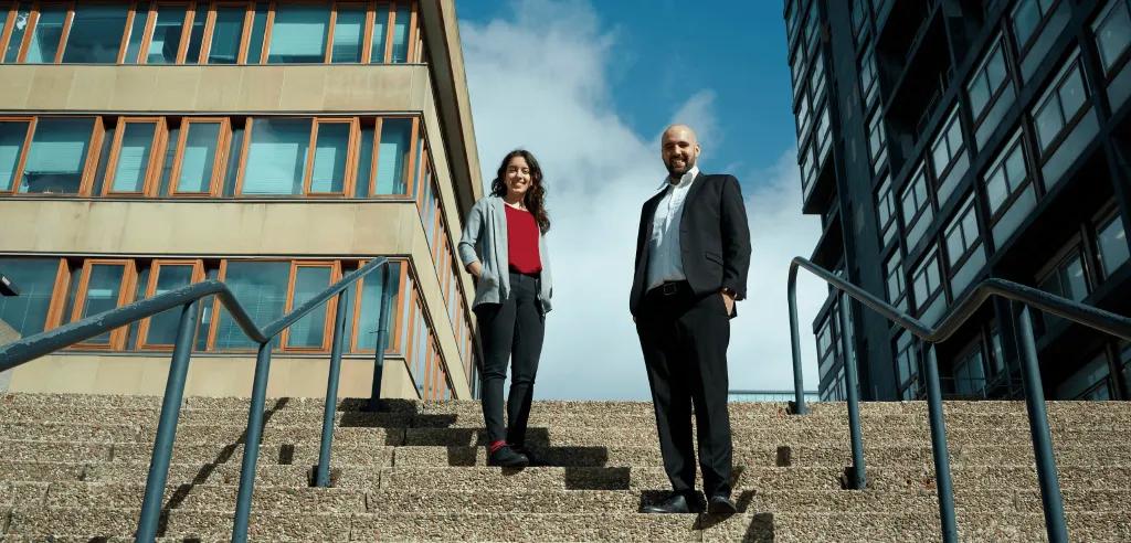 A woman and man stand on stairs with blue sky behind them. 