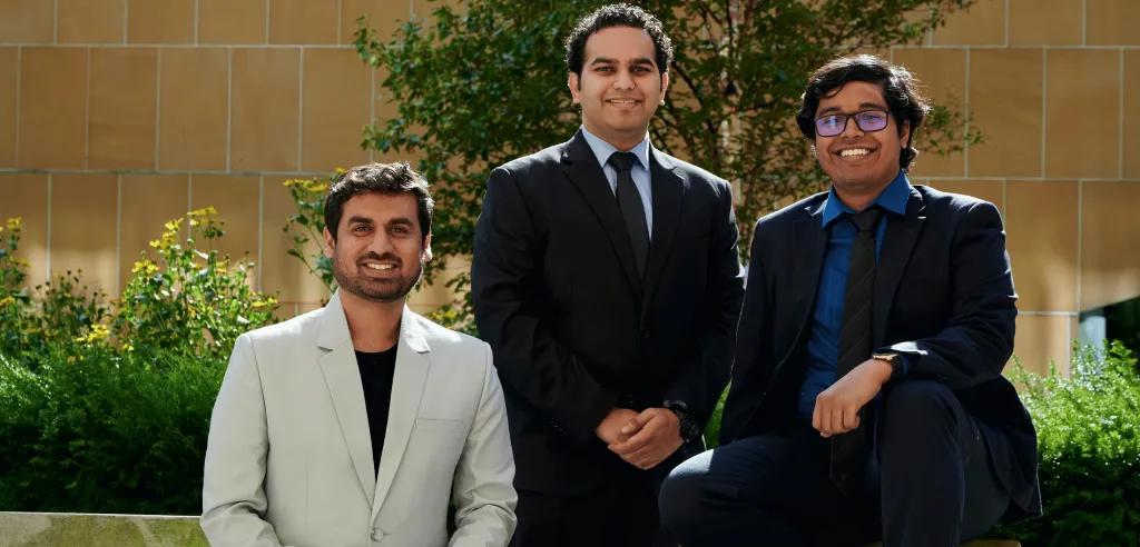 Three men, wearing suits, sat outside on a bench. 