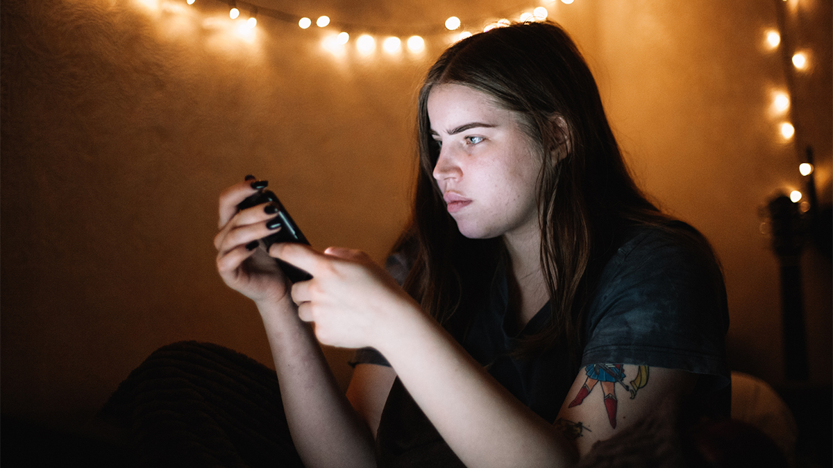 Teenager looking at their mobile phone in a dark room with fariy lights in the background.