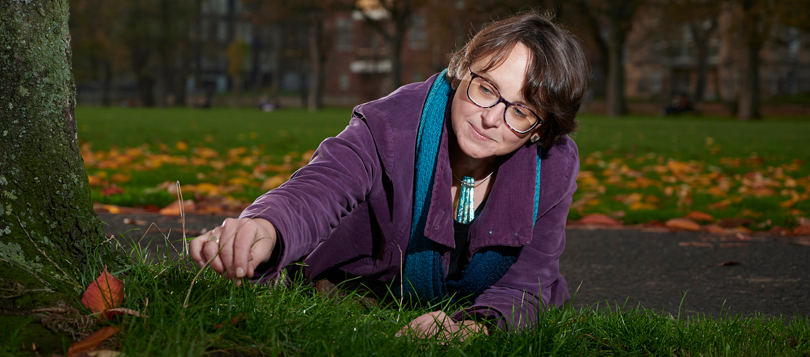 Image of Dr Tanja Romankiewicz looking closely at grass at the bottom of a tree