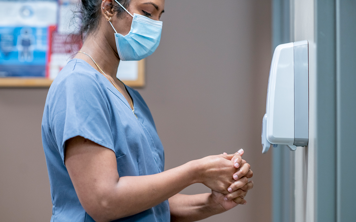 Woman in blue hospital scrubs, disinfecting her hands