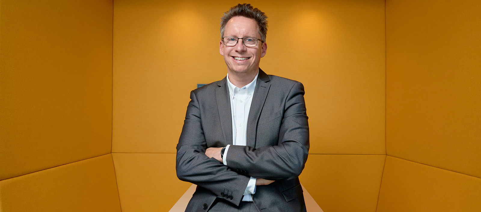 Image of Jonathan Fallowfield standing with his arms folded against a yellow background